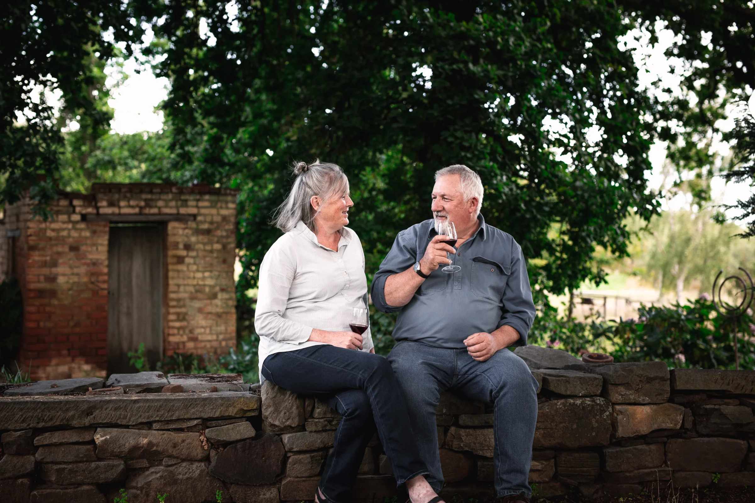 Two people sharing a glass of red wine on an old stone wall in the garden at Six Friends