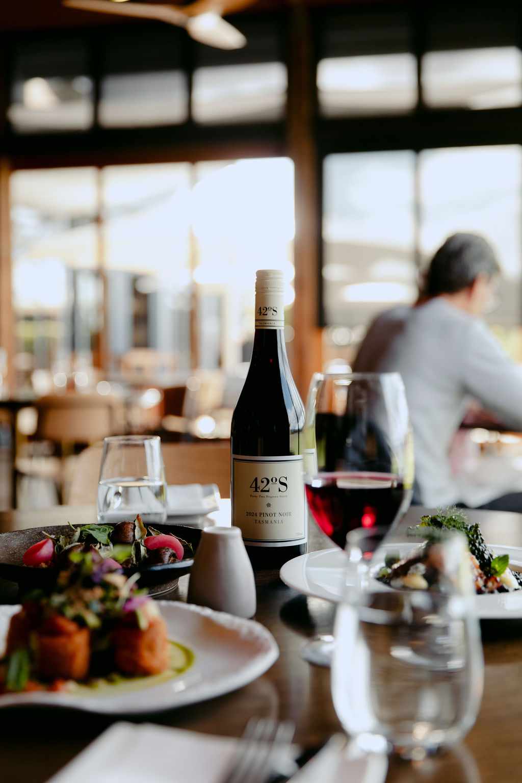 A bottle of Pinot Noir and a plated meal on a table in a Huon Valley cellar door restaurant